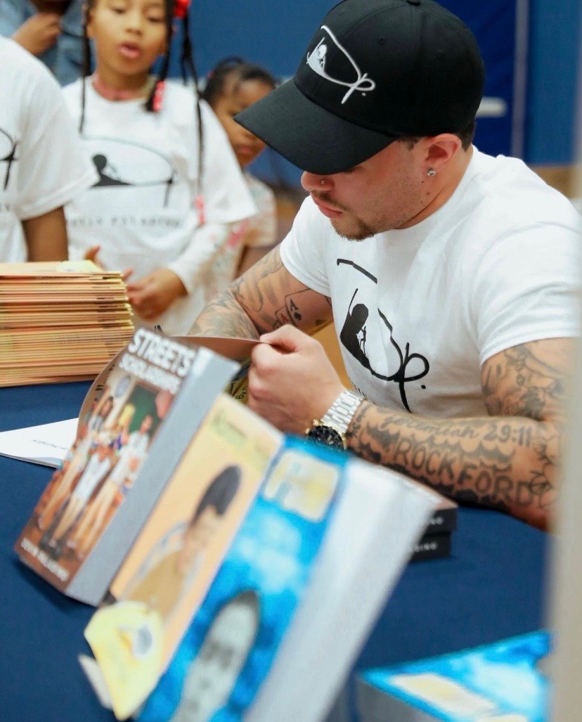 Devin Paladino signing a stack of his books at an event table