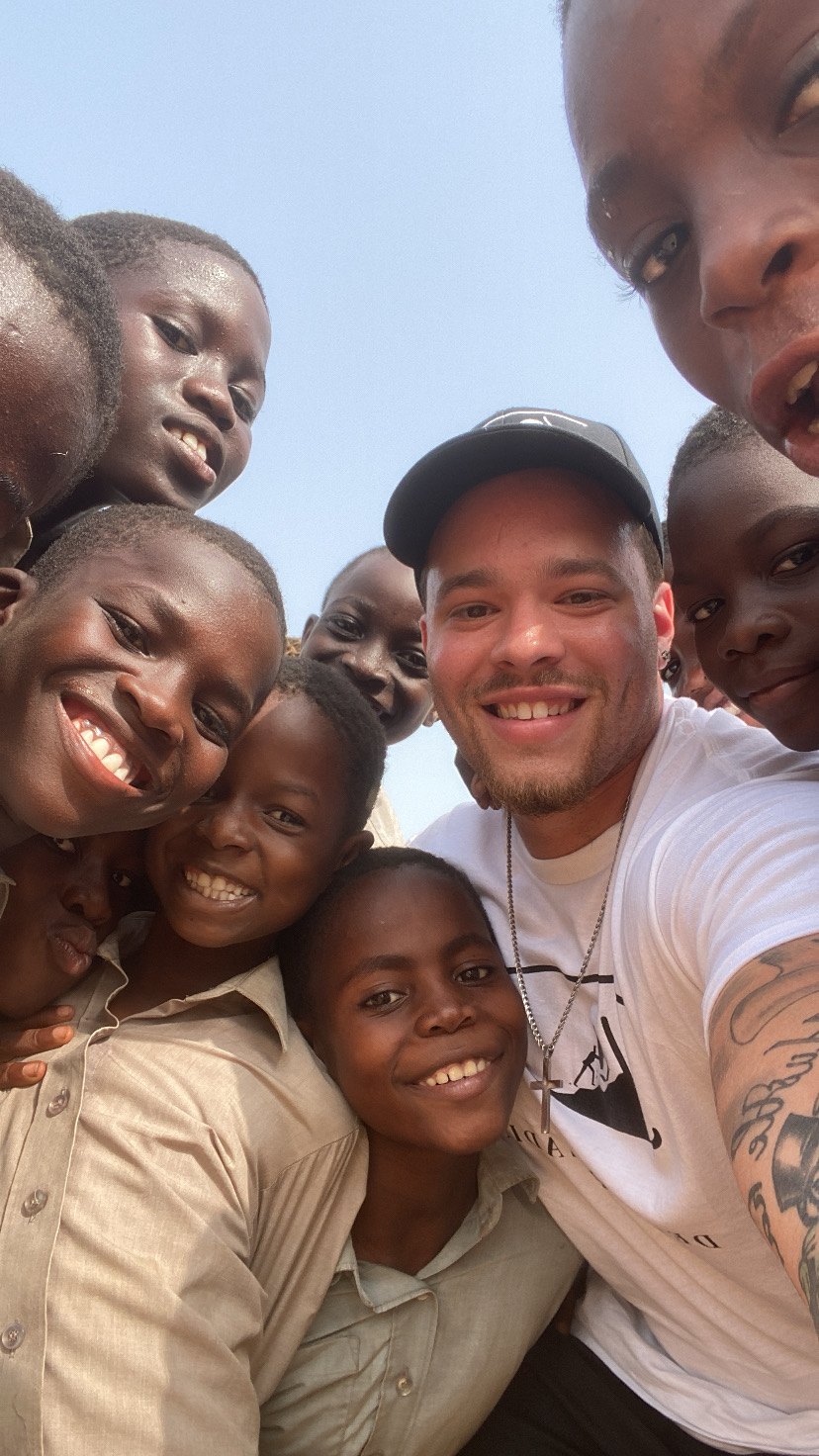 Devin Paladino taking a selfie with a group of smiling pupils in school uniform in Tema, Ghana