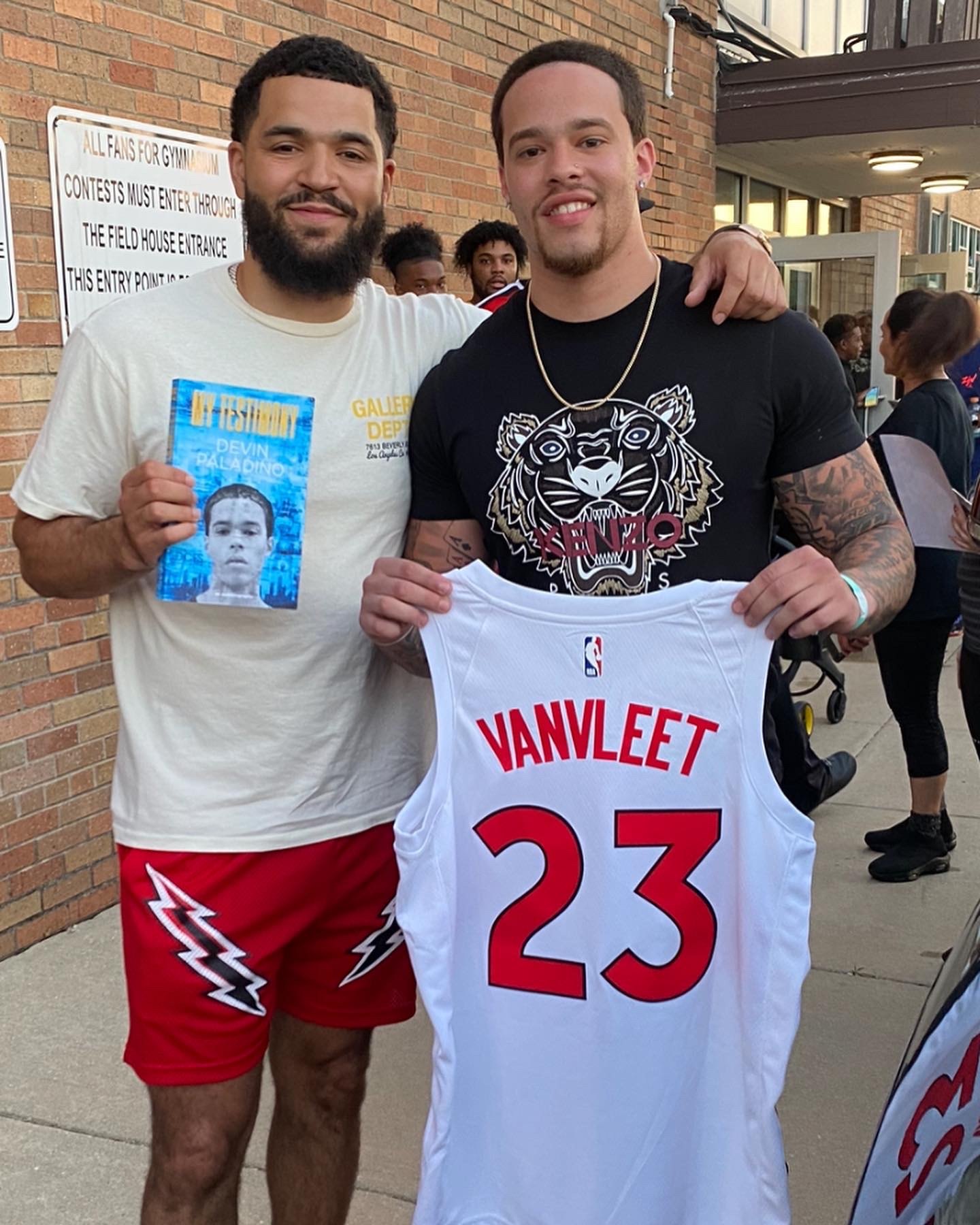Devin Paladino with an athlete holding a signed number 23 jersey and a copy of My Testimony