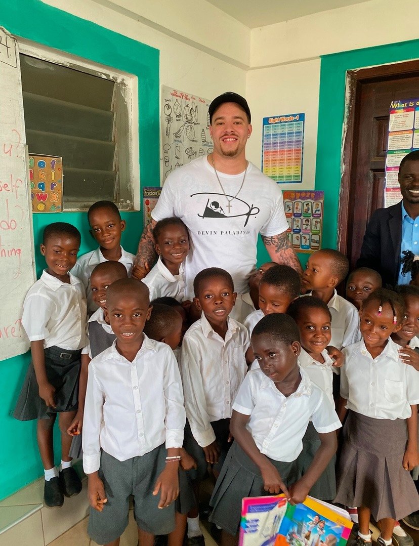 Devin Paladino at the back of a classroom in Tema, Ghana, with pupils in school uniform holding new books