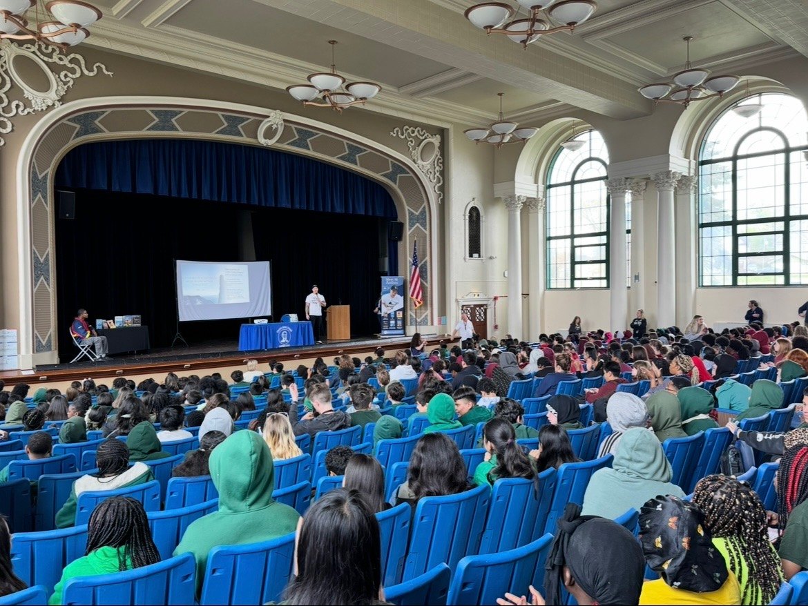A packed school auditorium of students facing the stage before a talk